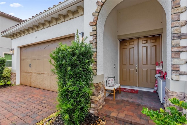 entrance to property featuring a garage, stone siding, and stucco siding