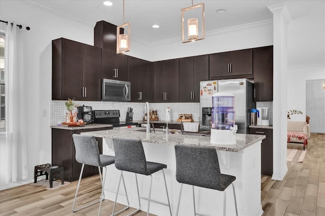 kitchen with light wood-type flooring, ornamental molding, appliances with stainless steel finishes, a breakfast bar area, and decorative backsplash