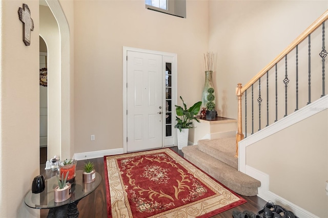 entrance foyer with wood finished floors, arched walkways, a high ceiling, baseboards, and stairs