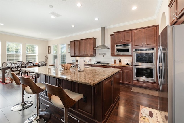 kitchen with decorative backsplash, appliances with stainless steel finishes, wall chimney exhaust hood, and ornamental molding