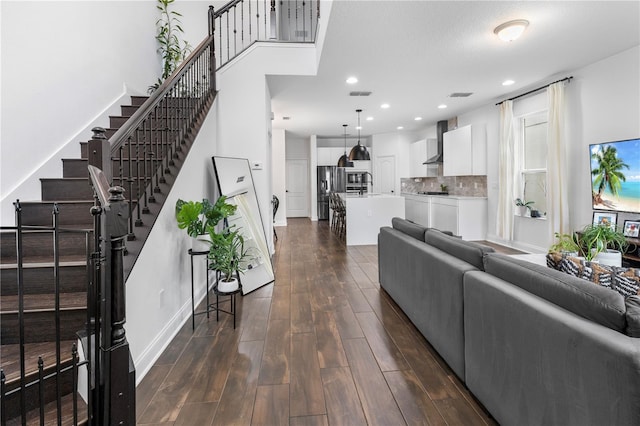 living room with dark wood-style floors, visible vents, baseboards, recessed lighting, and stairs