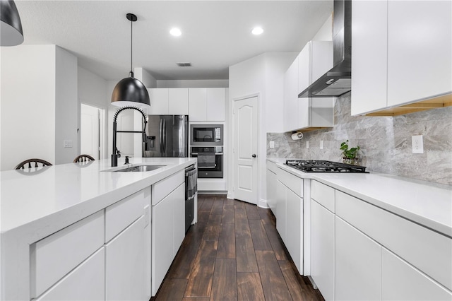kitchen featuring a sink, wall chimney range hood, backsplash, appliances with stainless steel finishes, and light countertops