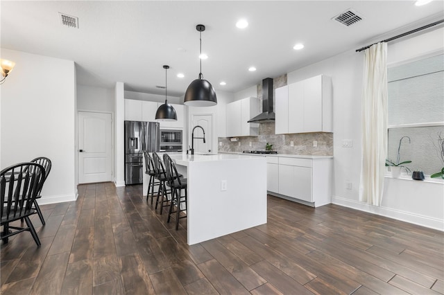 kitchen with wall chimney range hood, a breakfast bar area, visible vents, and stainless steel fridge with ice dispenser