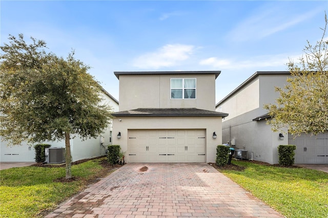 traditional home with central AC unit, stucco siding, an attached garage, and decorative driveway
