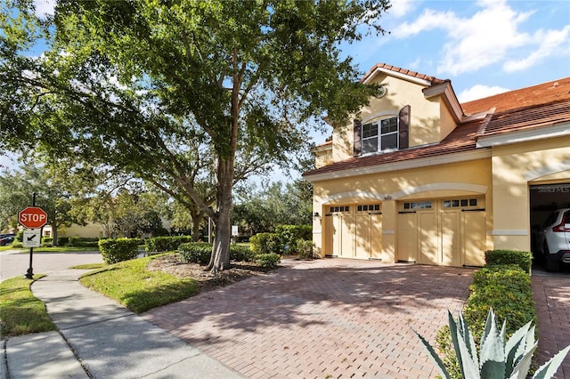 view of property exterior featuring a tile roof, decorative driveway, an attached garage, and stucco siding