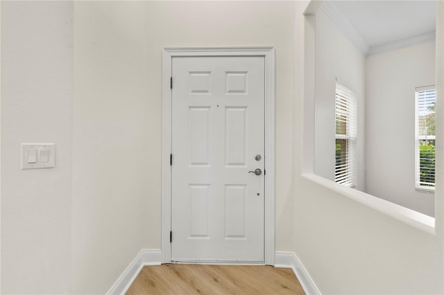 doorway featuring baseboards, ornamental molding, and light wood finished floors