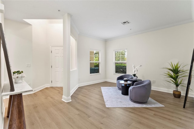 living area featuring visible vents, baseboards, light wood-style floors, and ornamental molding