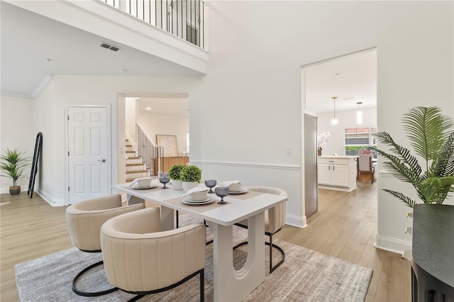 dining space featuring baseboards, visible vents, light wood finished floors, stairs, and a towering ceiling