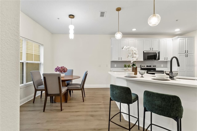 kitchen featuring a breakfast bar area, visible vents, stainless steel appliances, pendant lighting, and light wood-type flooring