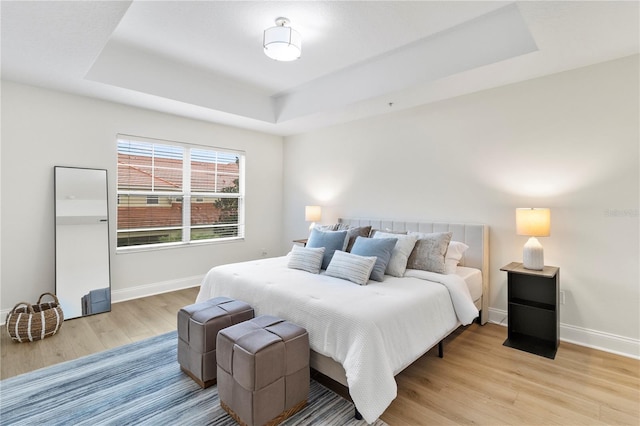 bedroom with a tray ceiling, baseboards, and light wood-style flooring