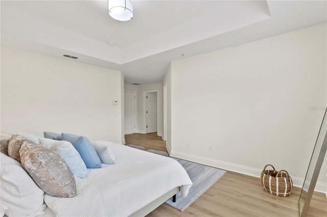 bedroom featuring visible vents, baseboards, a raised ceiling, and light wood finished floors