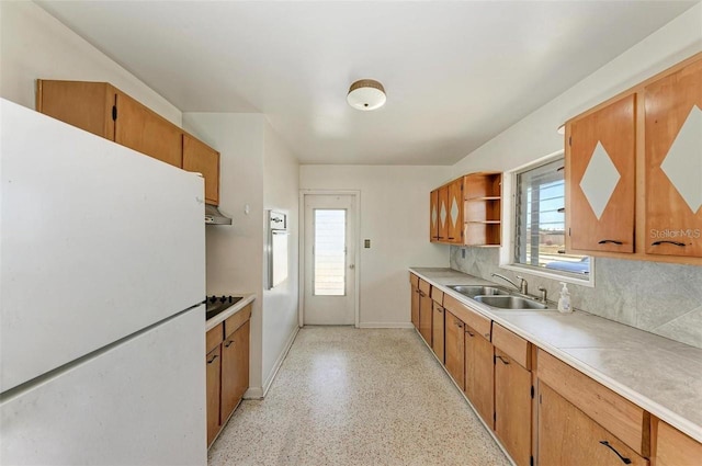 kitchen with brown cabinetry, open shelves, freestanding refrigerator, a sink, and light countertops