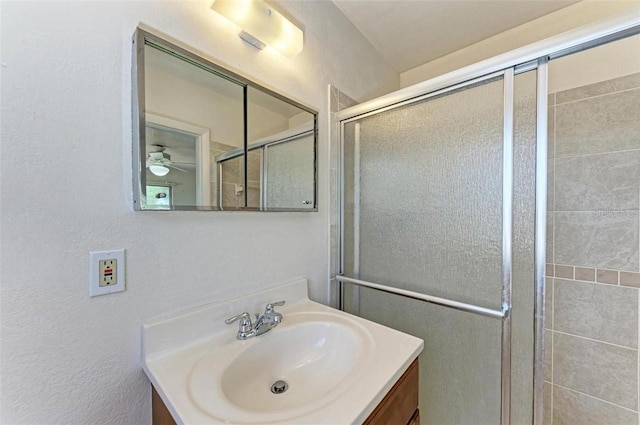 full bath with a textured wall, vanity, and a tile shower