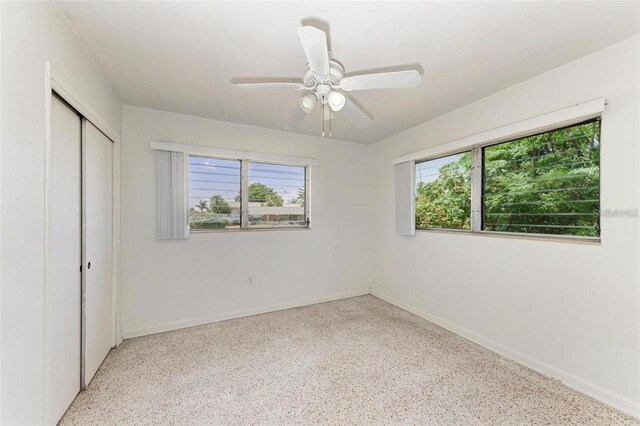 unfurnished bedroom featuring a closet, multiple windows, baseboards, and speckled floor