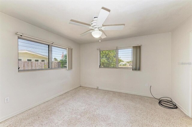 unfurnished room featuring a wealth of natural light, speckled floor, baseboards, and ceiling fan