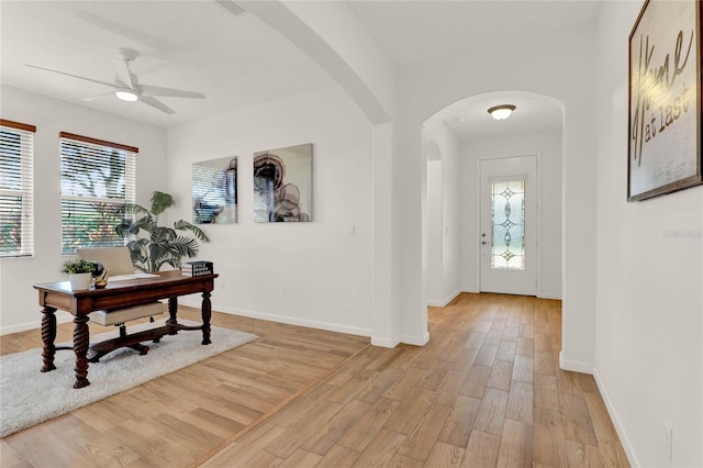 foyer entrance featuring a ceiling fan, baseboards, arched walkways, and light wood finished floors