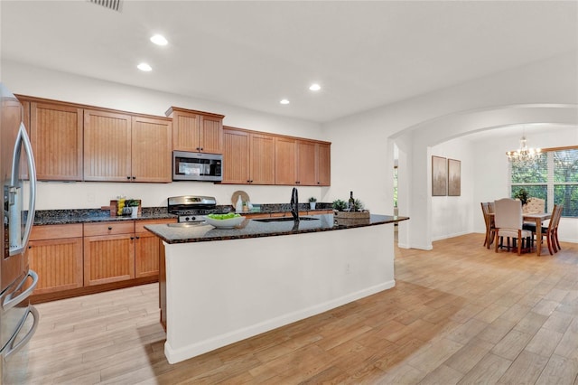 kitchen featuring light wood finished floors, arched walkways, stainless steel appliances, and a sink