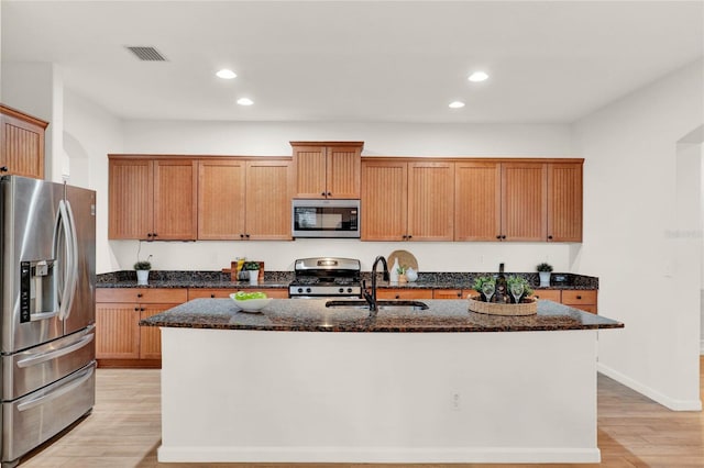 kitchen with an island with sink, appliances with stainless steel finishes, light wood-type flooring, and a sink