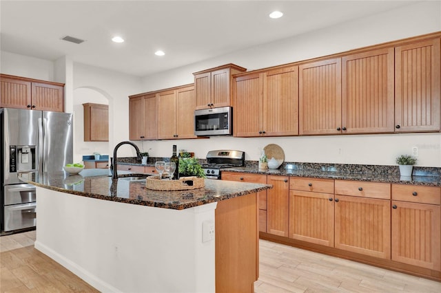 kitchen featuring dark stone countertops, visible vents, a kitchen island with sink, a sink, and appliances with stainless steel finishes