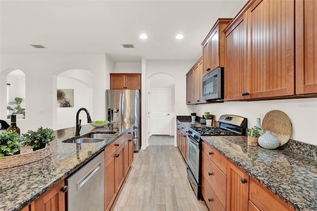 kitchen with a sink, stainless steel appliances, visible vents, and dark stone counters