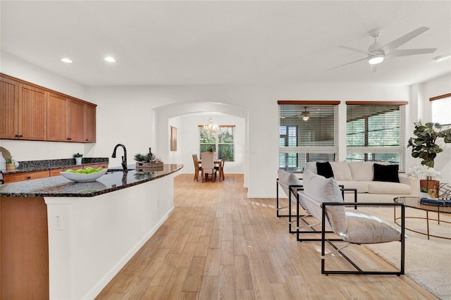 kitchen with brown cabinets, light wood-style flooring, dark stone countertops, recessed lighting, and arched walkways