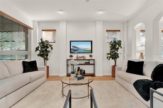 living room featuring baseboards, arched walkways, and light wood-style floors