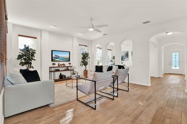 living area with visible vents, arched walkways, light wood-style floors, baseboards, and ceiling fan