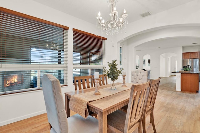 dining area featuring visible vents, a notable chandelier, arched walkways, light wood finished floors, and baseboards