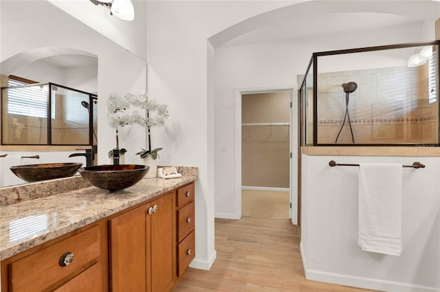 full bathroom with wood finished floors, a shower stall, baseboards, a spacious closet, and vanity