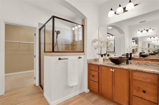 full bathroom featuring visible vents, a walk in closet, a stall shower, wood finished floors, and vanity