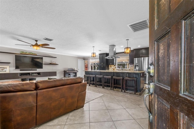 living room featuring light tile patterned floors, a ceiling fan, visible vents, and a textured ceiling