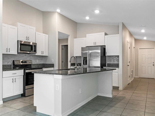 kitchen featuring light tile patterned floors, a center island with sink, a sink, vaulted ceiling, and appliances with stainless steel finishes