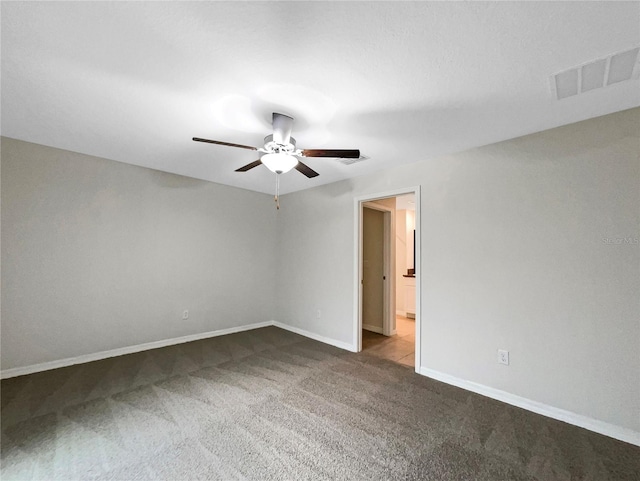 carpeted empty room featuring visible vents, a ceiling fan, and baseboards