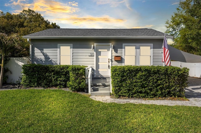 view of front facade with a shingled roof, a front lawn, and fence