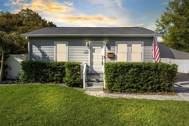 view of front facade with a shingled roof, a front lawn, and fence