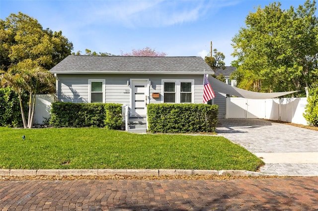 bungalow-style home with a gate, fence, roof with shingles, a front lawn, and decorative driveway