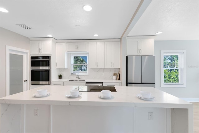 kitchen featuring visible vents, a kitchen island, white cabinets, stainless steel appliances, and a sink