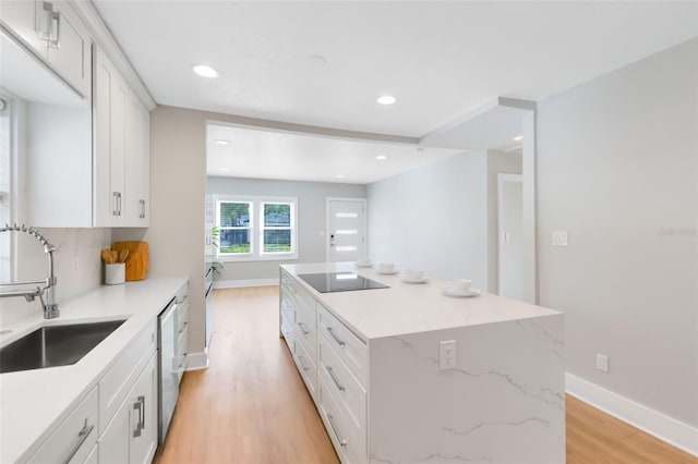 kitchen featuring light wood-type flooring, a sink, a center island, baseboards, and black electric stovetop