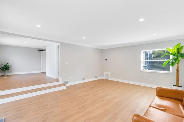 unfurnished living room with a barn door, baseboards, visible vents, and light wood-style flooring