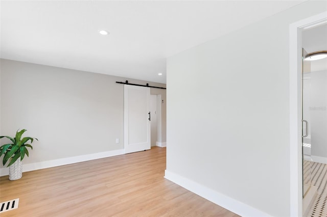 spare room with baseboards, light wood finished floors, visible vents, recessed lighting, and a barn door