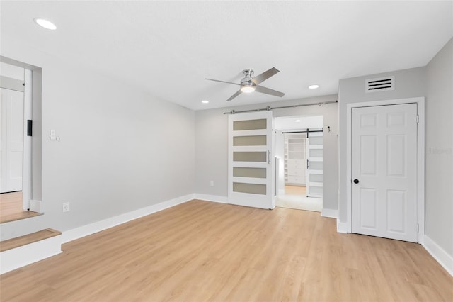 interior space with light wood-type flooring, visible vents, recessed lighting, a barn door, and baseboards