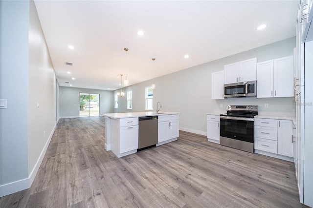 kitchen featuring a sink, stainless steel appliances, white cabinets, light wood-style floors, and open floor plan