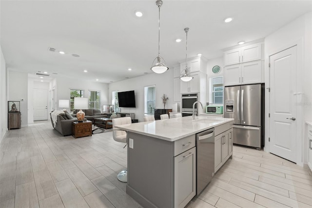 kitchen with wood finish floors, an island with sink, a sink, appliances with stainless steel finishes, and white cabinets