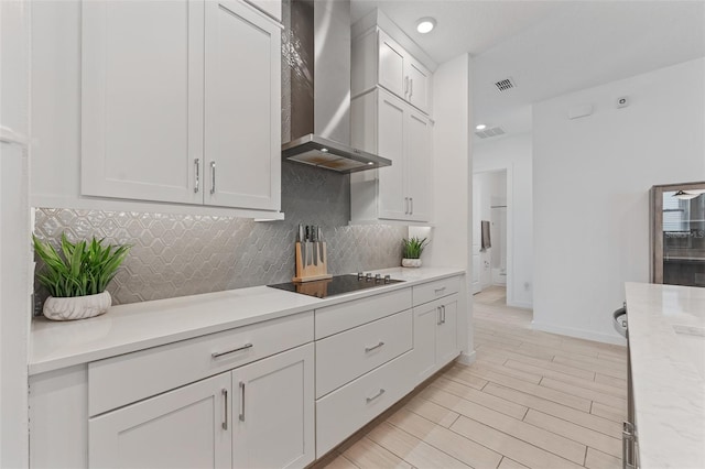 kitchen featuring visible vents, black electric stovetop, light countertops, wall chimney range hood, and tasteful backsplash