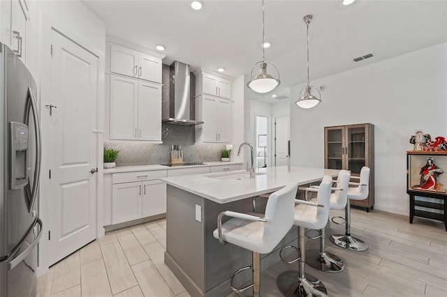 kitchen with visible vents, decorative backsplash, wall chimney exhaust hood, black electric cooktop, and stainless steel fridge