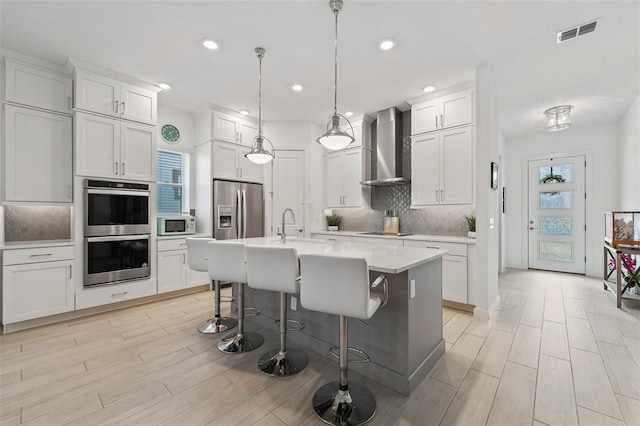 kitchen with visible vents, wall chimney range hood, a kitchen bar, light countertops, and stainless steel appliances