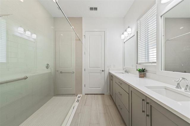 full bath with double vanity, visible vents, a tile shower, and a sink