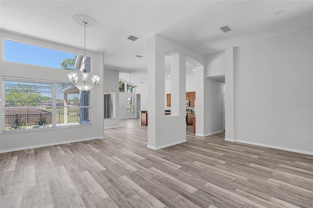 unfurnished living room featuring a high ceiling, light wood-style floors, visible vents, and baseboards