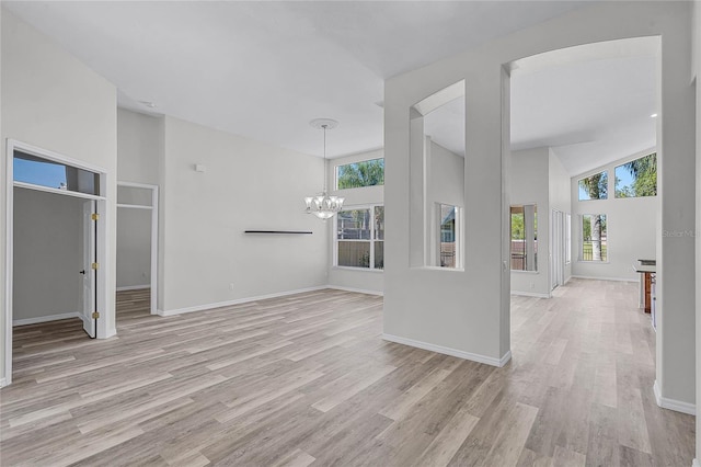 unfurnished living room with a wealth of natural light, light wood-type flooring, high vaulted ceiling, and an inviting chandelier