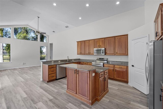 kitchen featuring dark stone countertops, high vaulted ceiling, a peninsula, stainless steel appliances, and brown cabinets